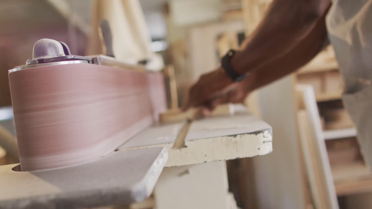 sezione centrale di un falegname maschio afroamericano che usa una macchina di levigatura a cintura per lucidare il legno