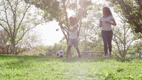 slow motion shot of mother and daughter playing soccer in park together