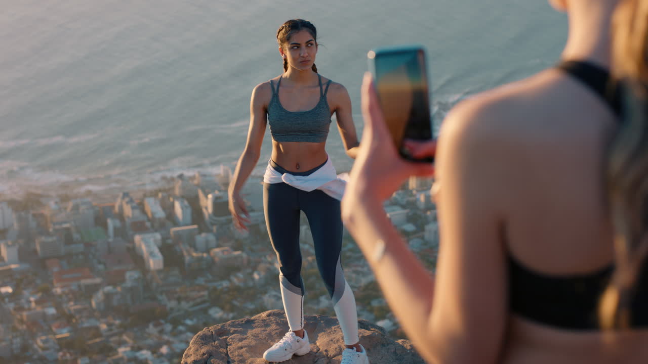 amigas tomando fotos en la cima de la montaña usando la cámara del teléfono inteligente feliz joven influencer mujer posando para un amigo con el teléfono móvil compartiendo la aventura de senderismo en las redes sociales