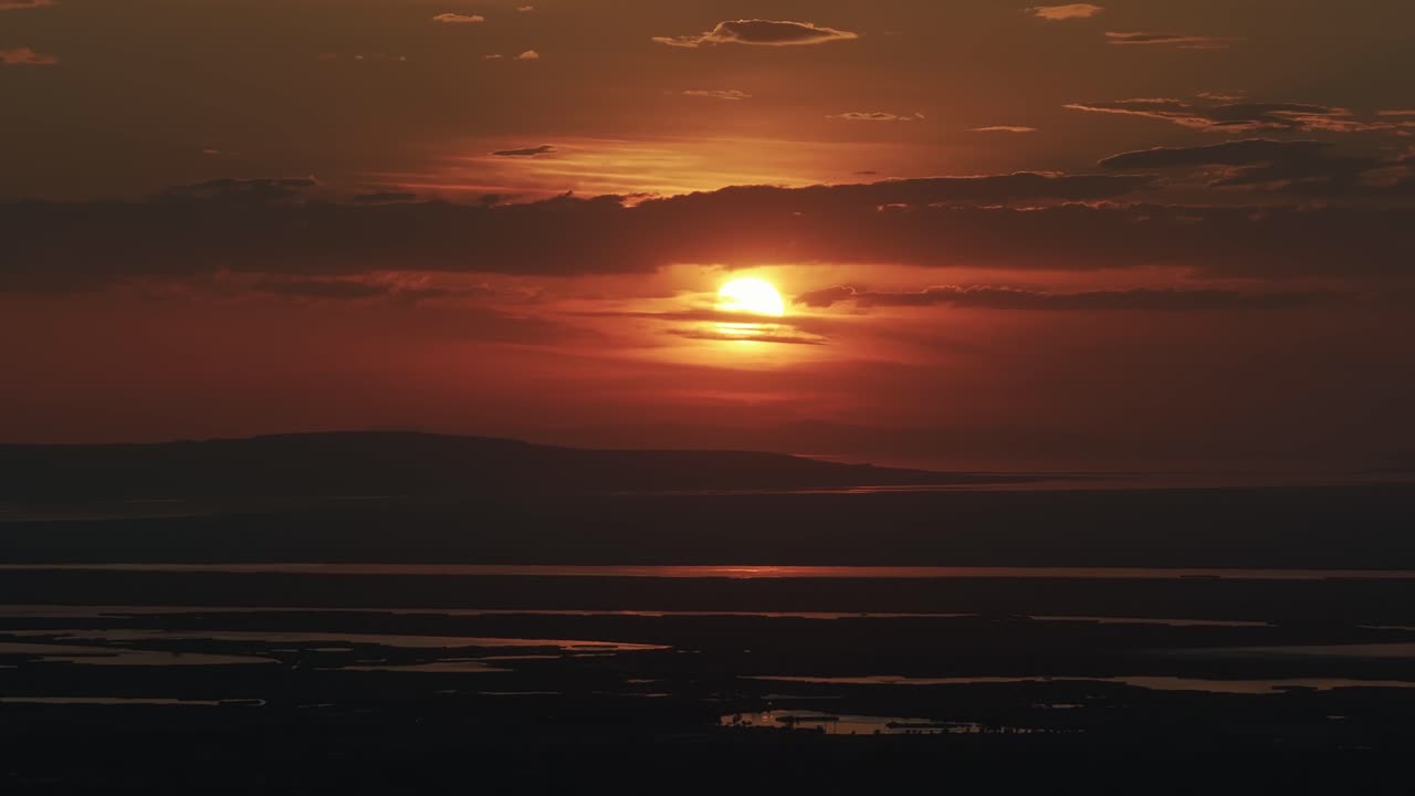 Drone view from Bountiful Canyon in Utah of a golden summer sunset over Salt Lake Valley with clouds, mountains, and water ponds reflecting light from the Great Salt Lake