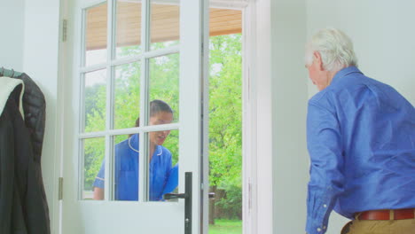 Senior-Man-At-Home-Using-Walking-Frame-Greeting-Female-Nurse-Or-Care-Worker-In-Uniform-At-Door