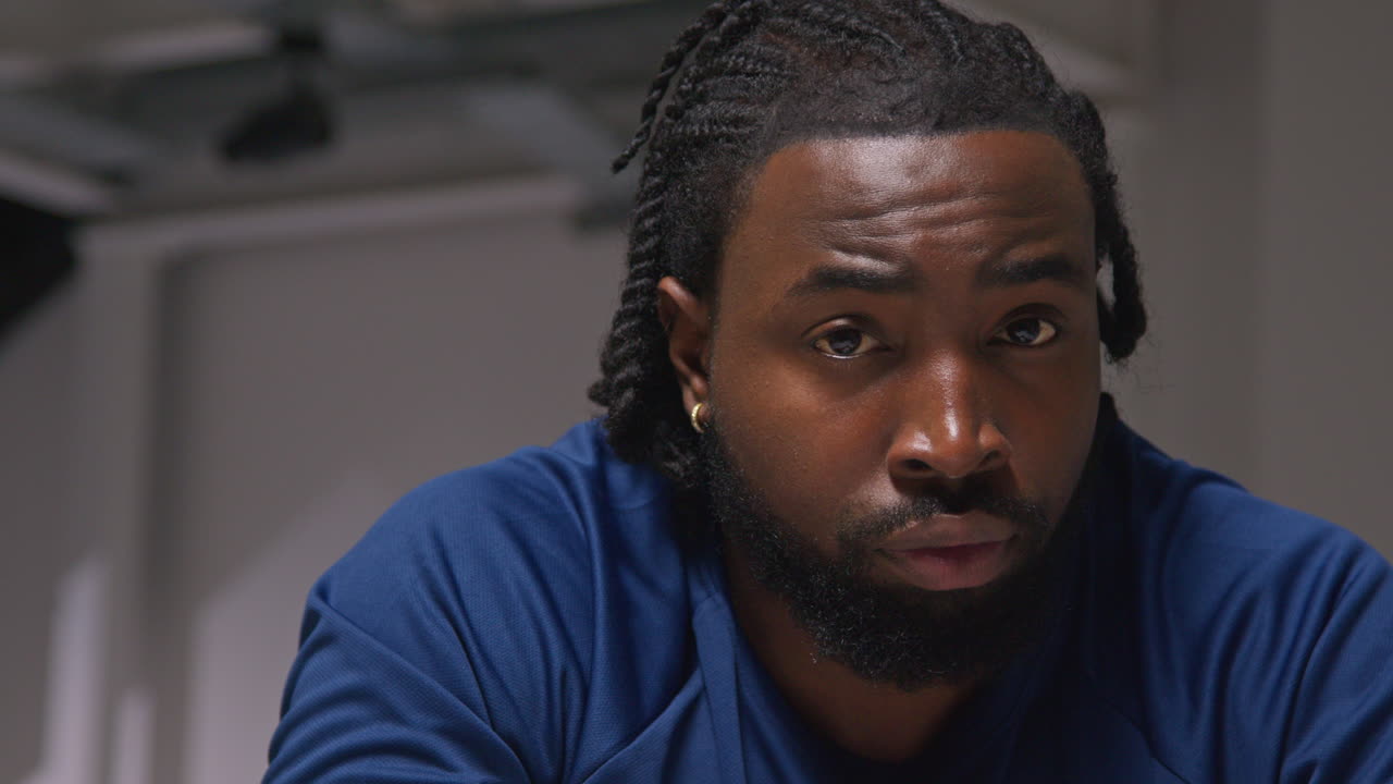 retrato de cerca de un atleta masculino decidido entrenando en el gimnasio sentado y concentrado en el vestuario con expresión enfocada 3