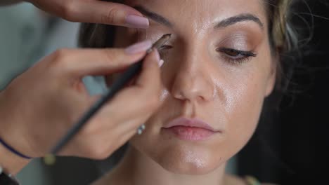 makeup artist outlining the eyes and eyelashes of bride