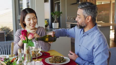 happy diverse couple sitting at table in dining room, eating dinner and drinking wine