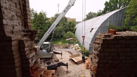 excavator and few men work in the yard of the constructed building. entering the room through the broken doorway with bricks in a pile.