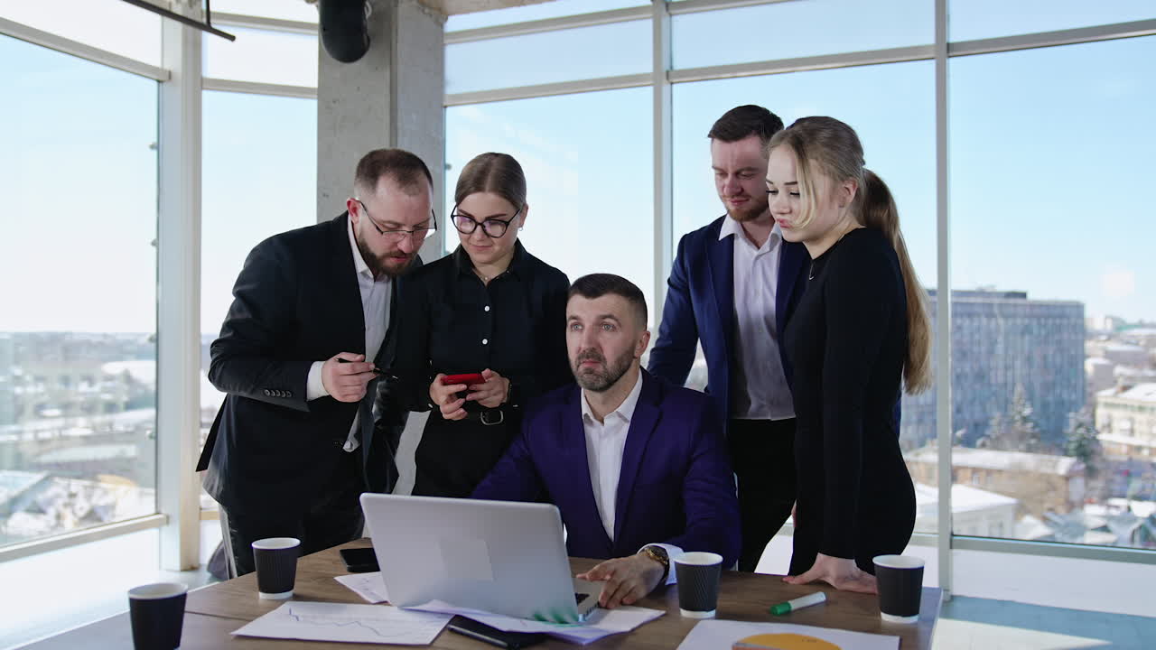 Businessman sits at the computer surrounded by his employees. Teammates sharing ideas and communicating for the best result.