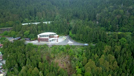 alishan national forest, showing dense green forests, roads, and a building, aerial view