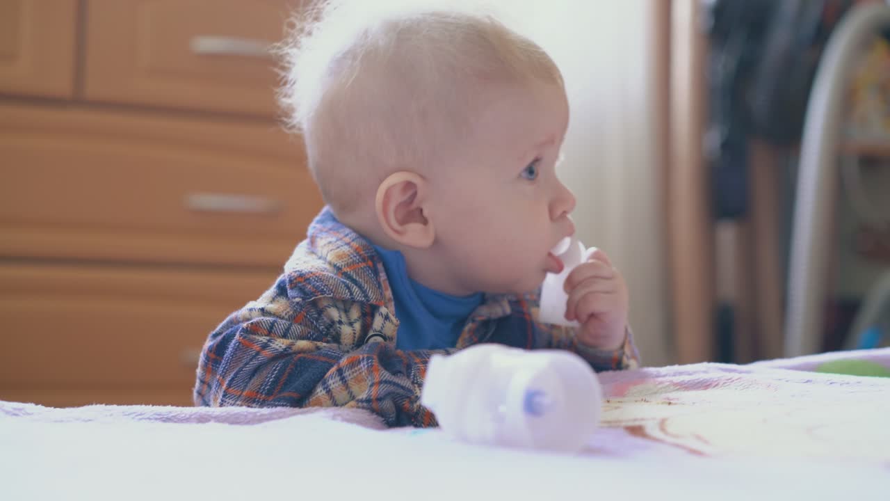 niño mordisquea parte del inhalador de pie cerca de la cama de cerca