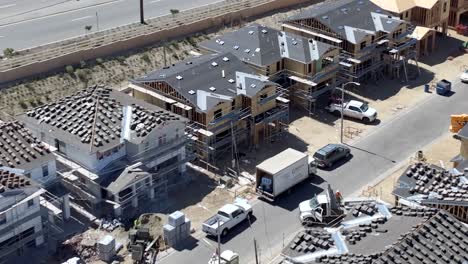 Aerial-view-dolly-across-new-build-housing-property-development-rooftops,-looking-down-over-construction-site