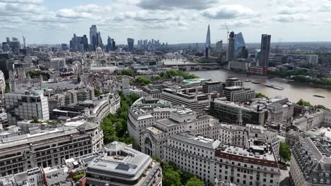 aerial view soaring southeast over somerset house and the temple gardens, revealing iconic blackfriars station and the shimmering river thames under cloudy skies.