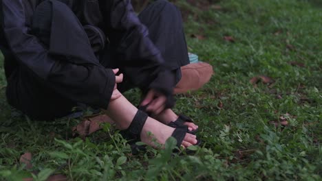 young woman putting on velcro sandals on feet in outdoor settings