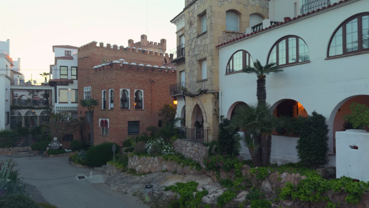 Scenic shot of traditional Mediterranean houses in Roc de Sant Gaietà at sunset. Historic facades, stone and brick buildings, palm trees and gardens create a peaceful coastal scene