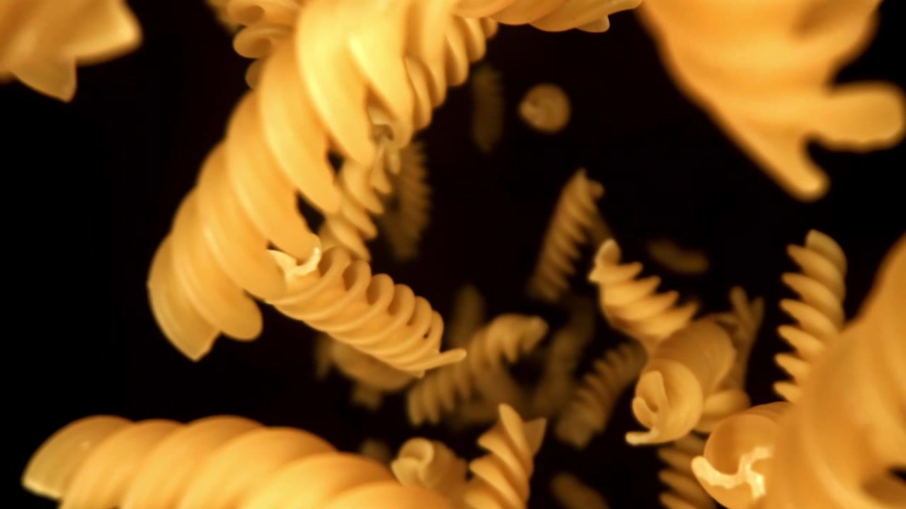 Pasta fusilli cruda che cade al rallentatore su sfondo nero