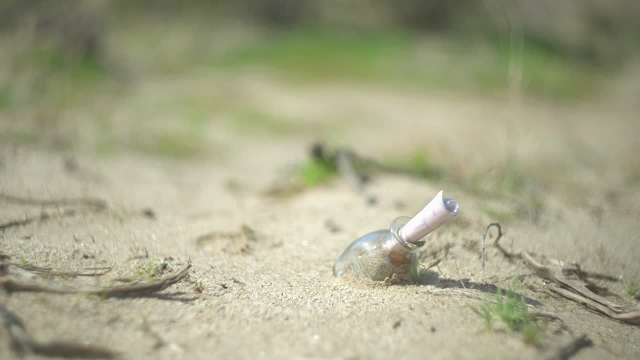 사막의 바닥에 있는 병에 담긴 메모, 그 주변에 초록색 식물이 있는 황금 모래에 혀 있는 메모.