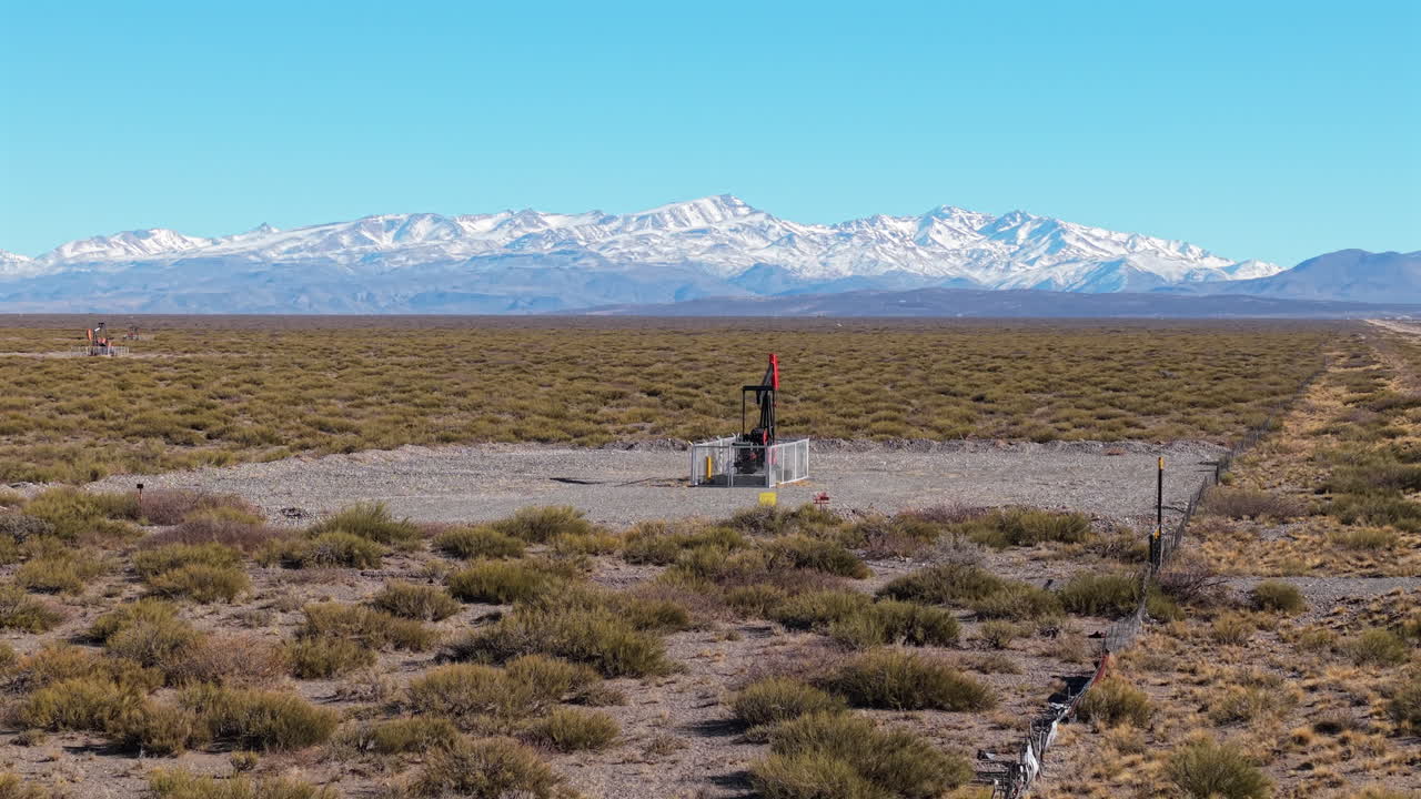 Movimento di avvicinamento del drone a una pompa di estrazione petrolifera e montagne innevate in un paesaggio arido, Mendoza, Argentina.