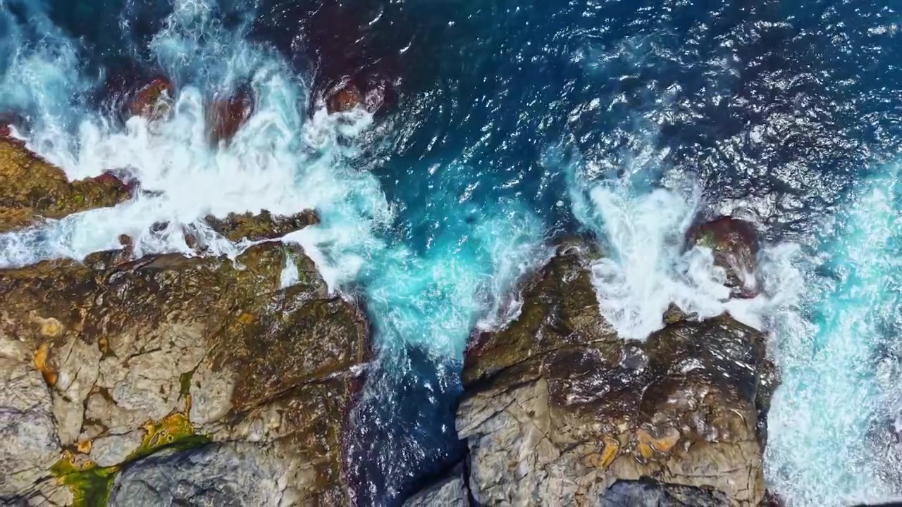 Wellen, die tagsüber an einer felsigen Küste mit leuchtend blauem Wasser brechen
