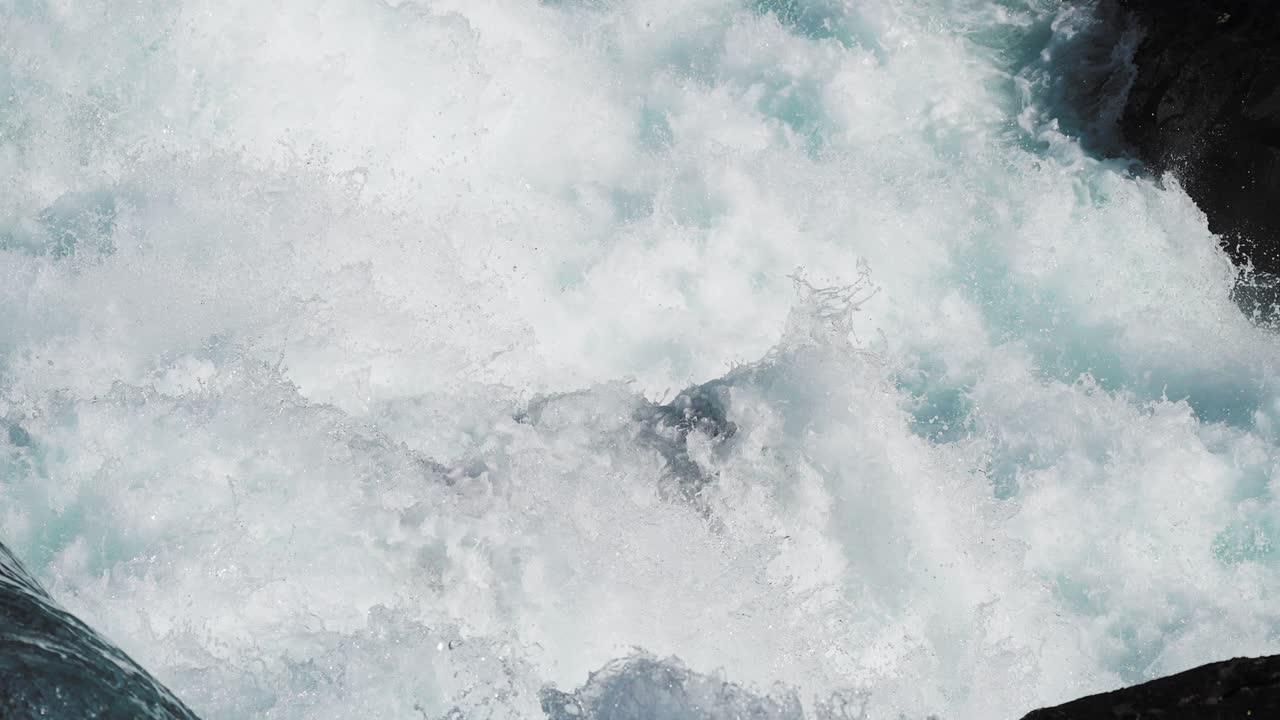 Close-up of a cascading waterfall, with whitewater tumbling and splashing over the dark rocky ledges into a pool below