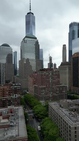 vertical drone footage rising high over s end ave., new york, offering a stunning aerial view of skyscrapers, streets, and the waterfront in an urban setting.