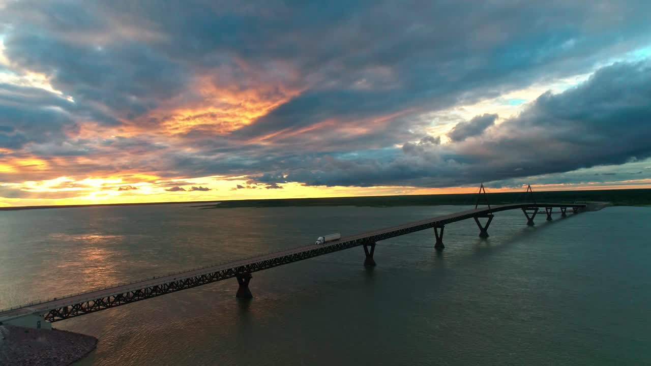 vista aérea de un camión que conduce sobre el puente deh cho al atardecer, cerca de los territorios del noroeste de fort providence - río mackenzie