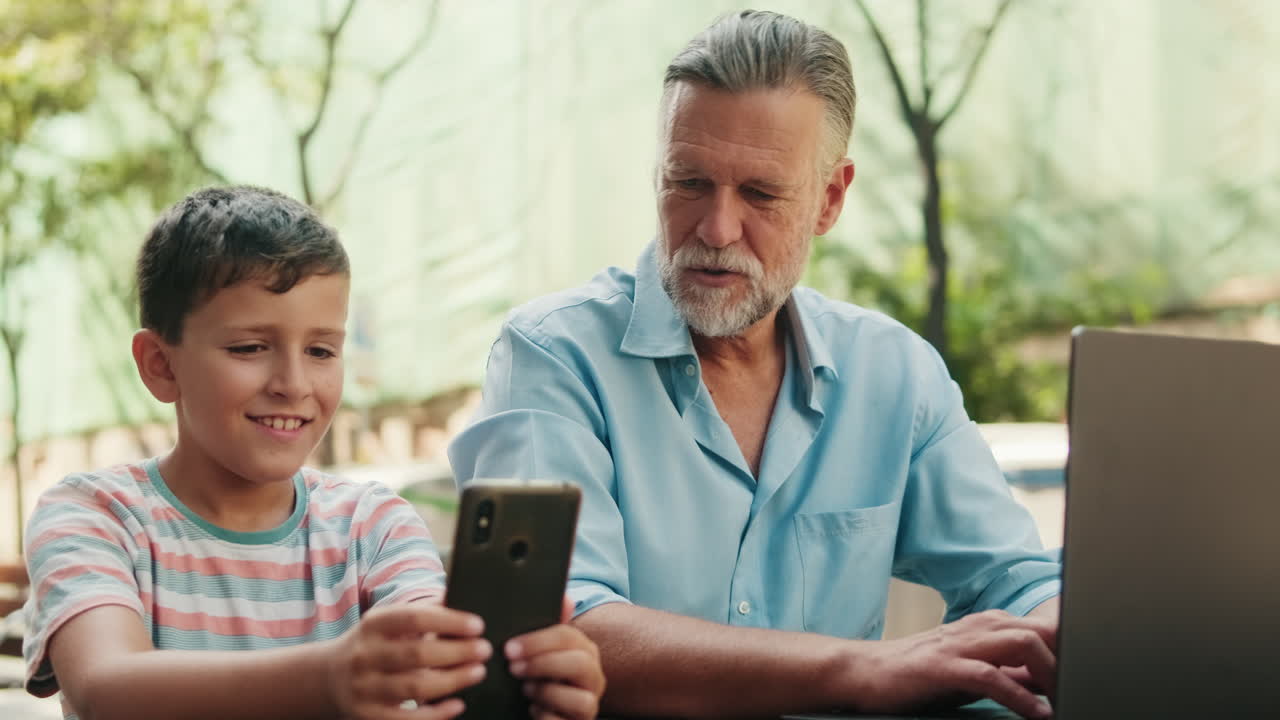 Happy Grandfather and Grandson Using Digital Devices Outdoors