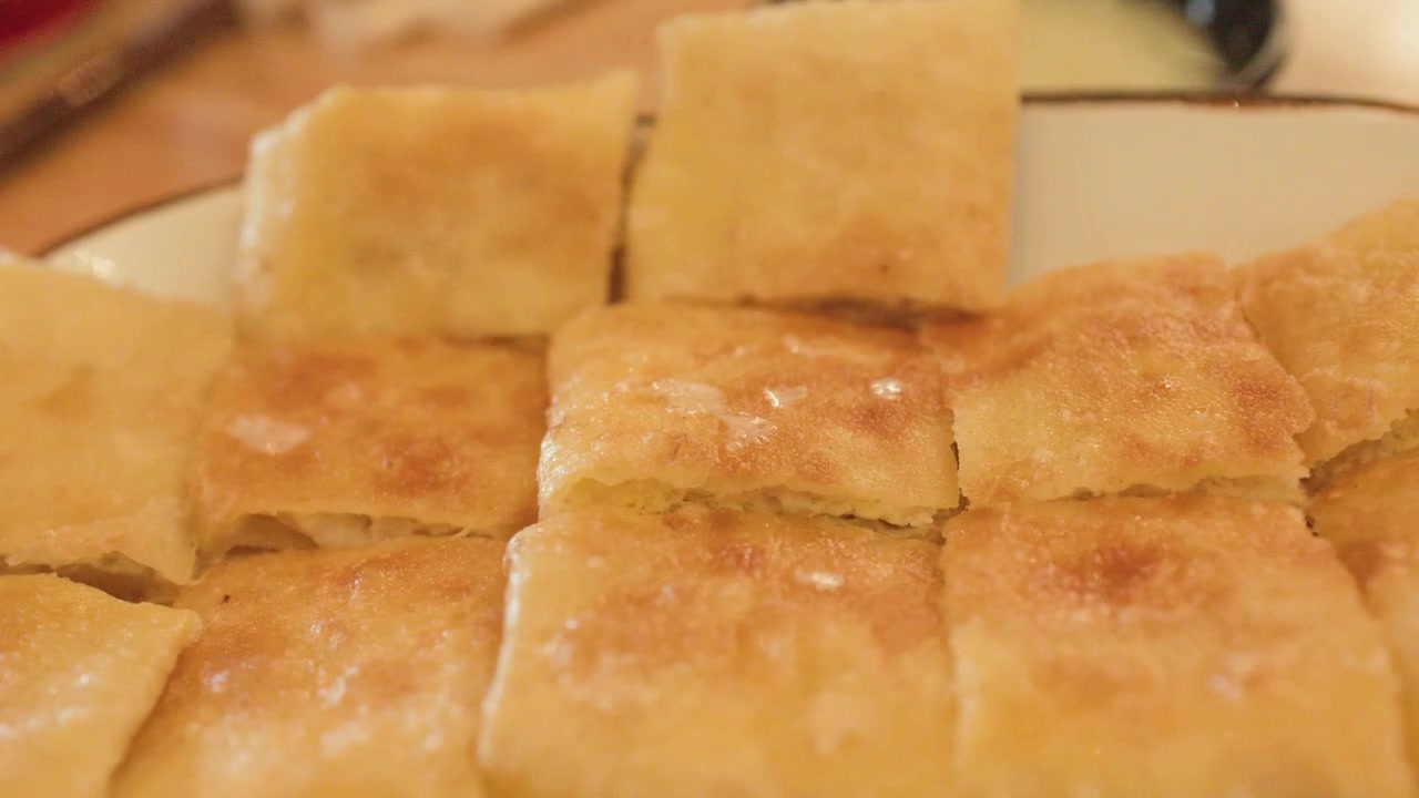 Primo piano di quadrati di pancake roti fritti dorati su un piatto bianco a Bangkok.