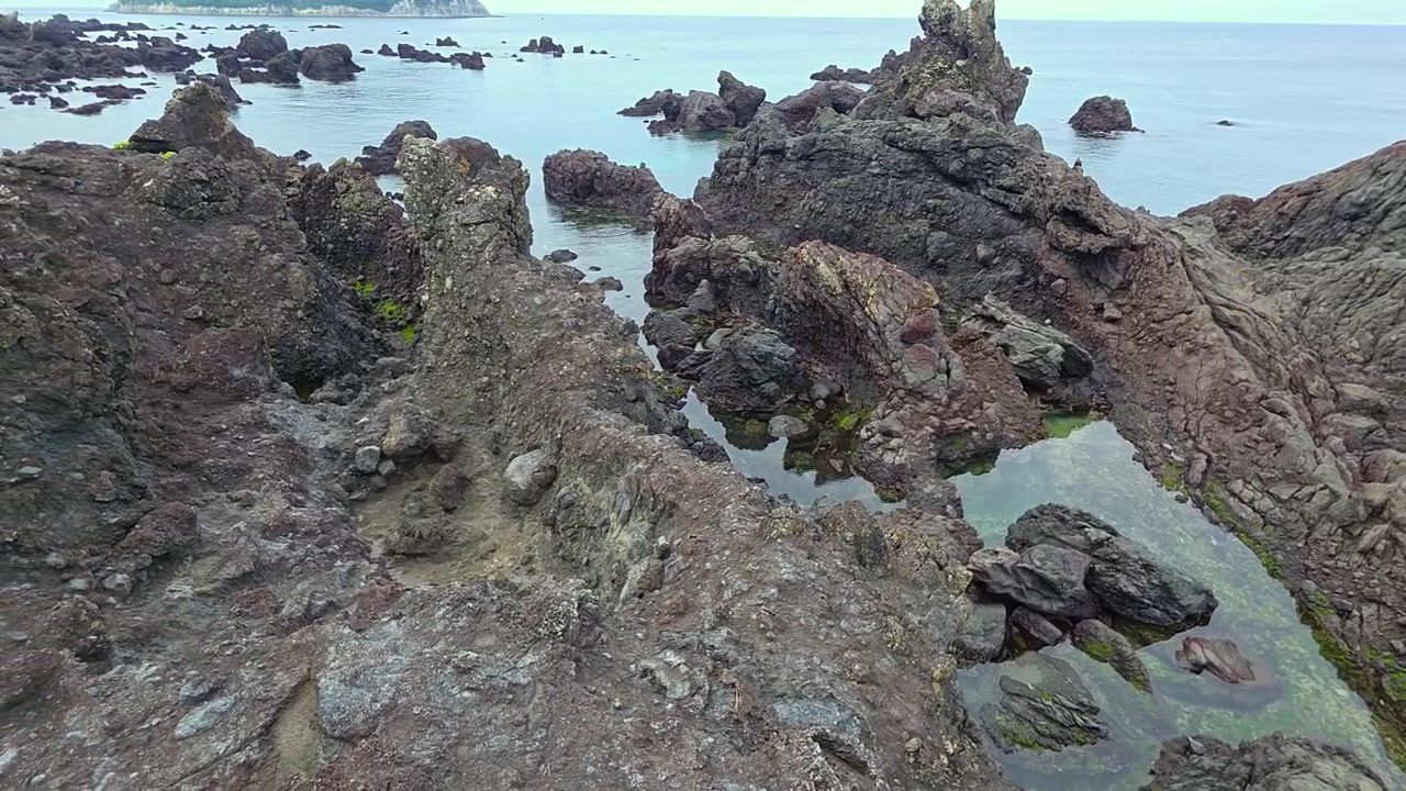 Un panoramique révèle des stacks volcaniques déchiquetés et une baie turquoise calme le long d'une côte rocheuse accidentée près du réservoir de Socheon Ji, Jeju.