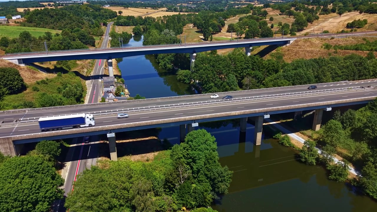 Ponte rodoviária da Autoestrada L'Armoricaine transporta tráfego em movimento sobre o Rio Mayenne em Change, Mayenne, Pays de la Loire, França, ao lado de uma ponte rodoviária secundária, sobrevoo lento de drone para a frente