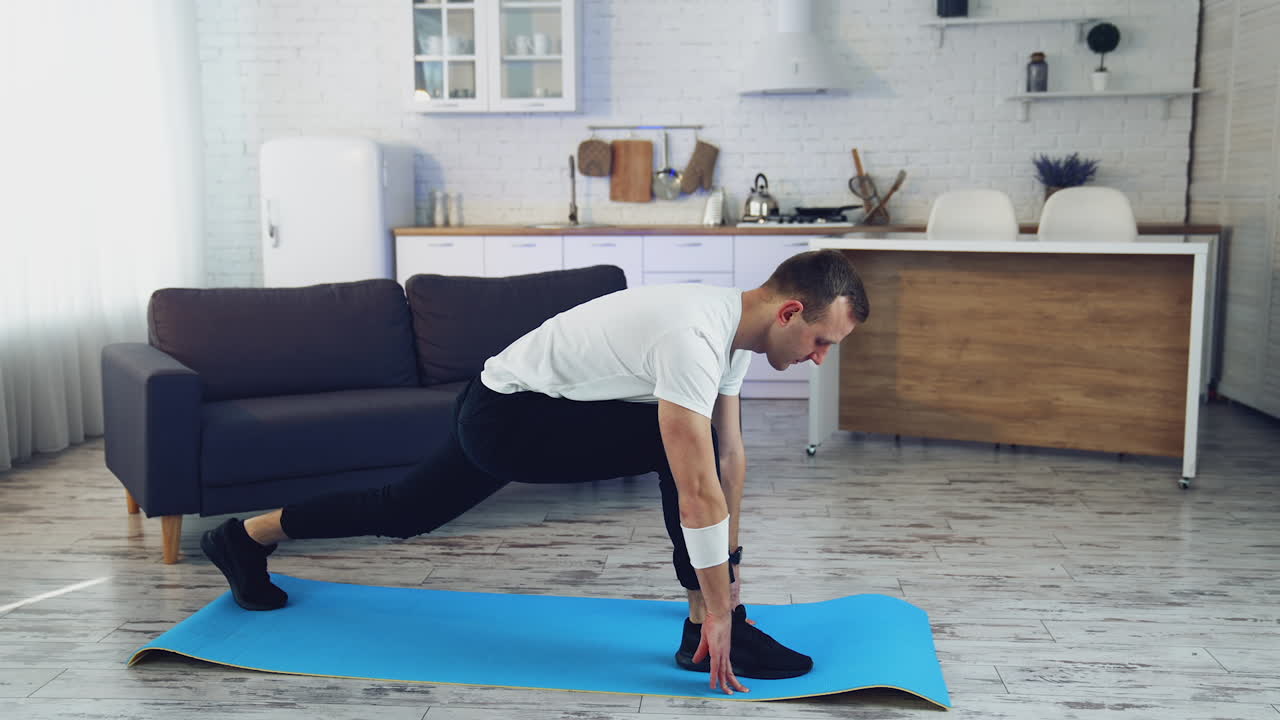 Young man doing fitness at home. Man in t-shirt and pants is doing exercises on mat at home in his spacious kitchen.