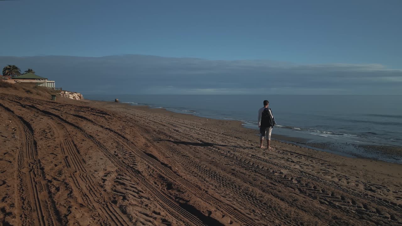 mochilero mirando el horizonte de la playa, parado, cámara moviéndose a su alrededor