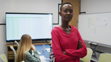 Portrait-of-african-american-businesswoman-smiling-in-office,-with-colleague-working-in-background