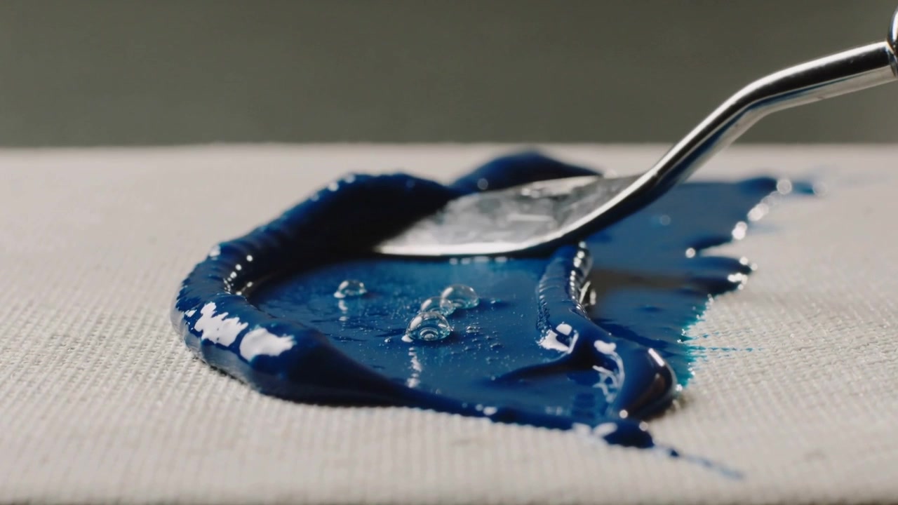 Una spatola metallica preme nella pittura blu su tela, stendendo il colore per modellare il bordo.