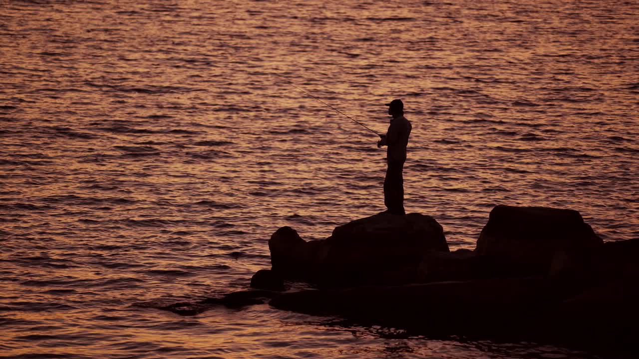 Fishermen on the rocks. Man's silhouette fishing at sunset. Freshwater fishing, catch of fish.