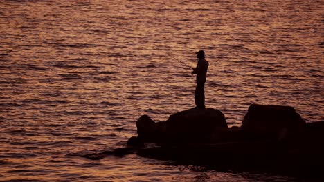 fishermen on the rocks. man's silhouette fishing at sunset. freshwater fishing, catch of fish.