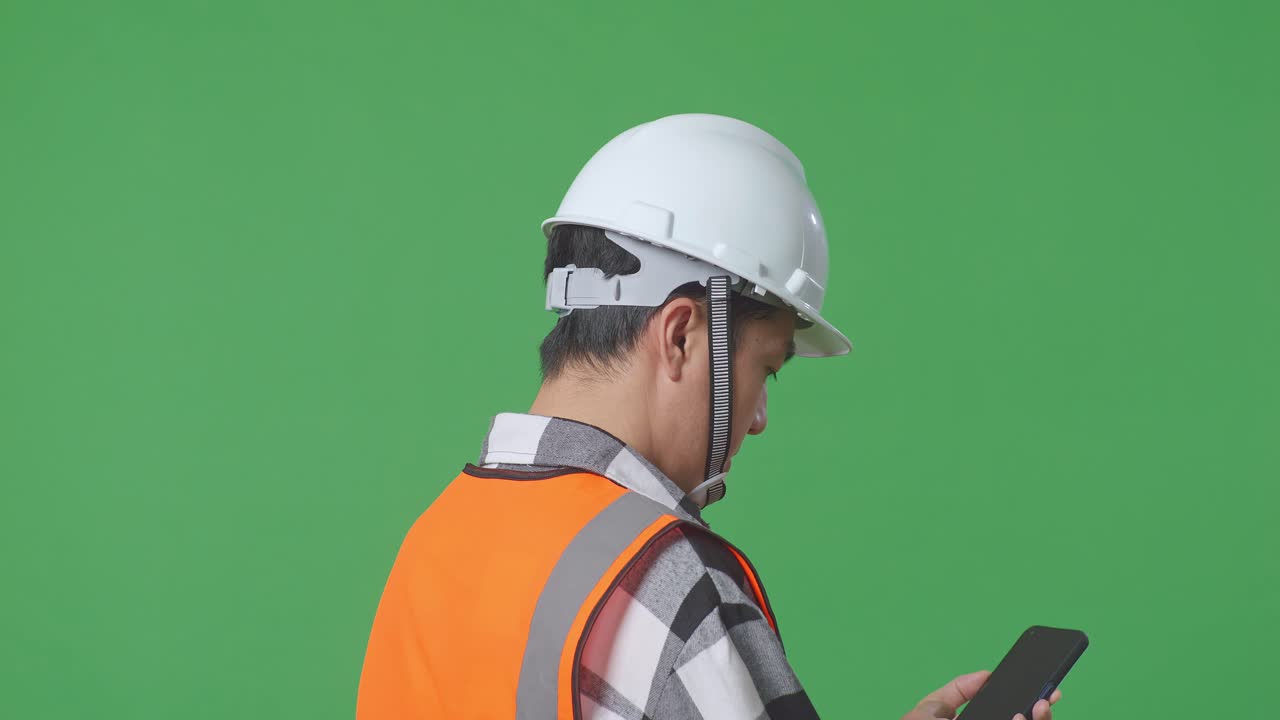 Close Up Back View Of Asian Male Engineer With Safety Helmet Talking On Smartphone While Standing In The Green Screen Background Studio