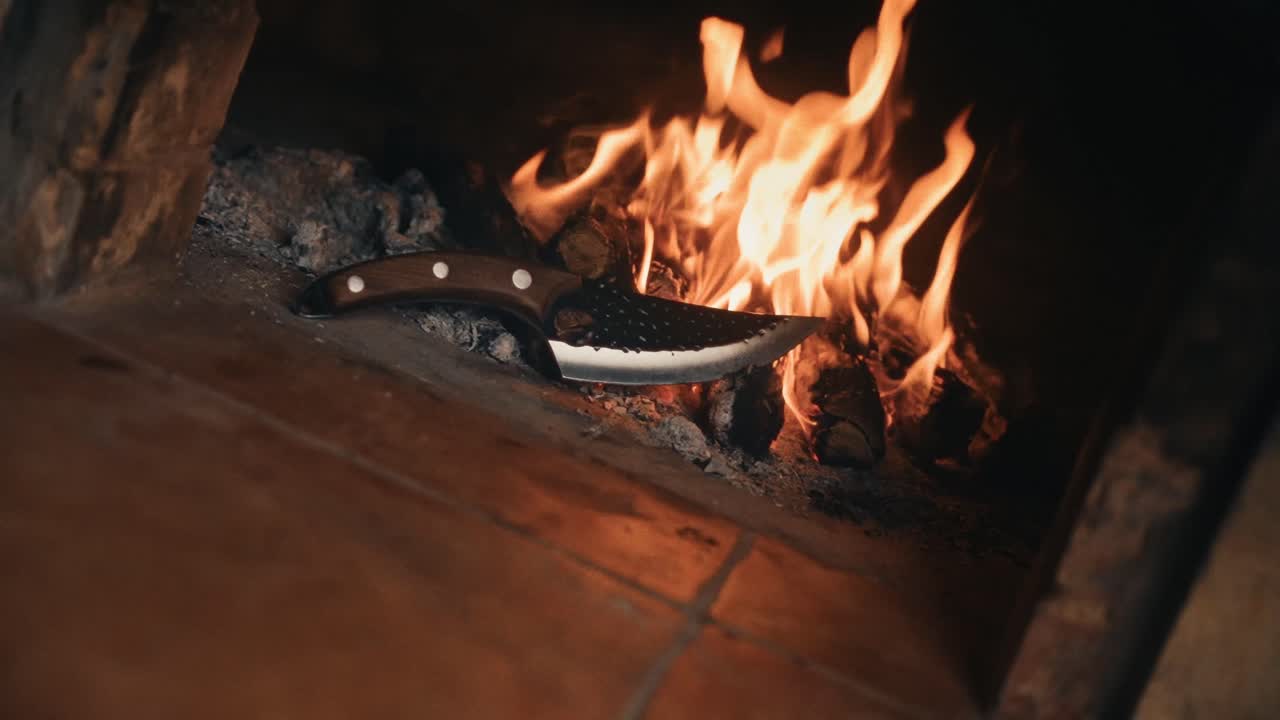 A burning knife lies in embers, evoking craftmanship and the forging process.