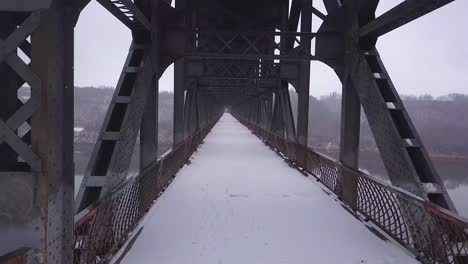 Winter-snow-falls-onto-unused-old-steel-truss-bridge-over-wide-river