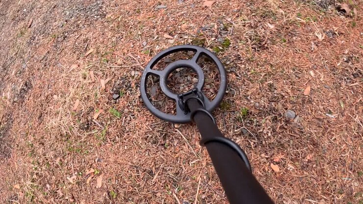 Metal detector moves over sparsely turfed ground