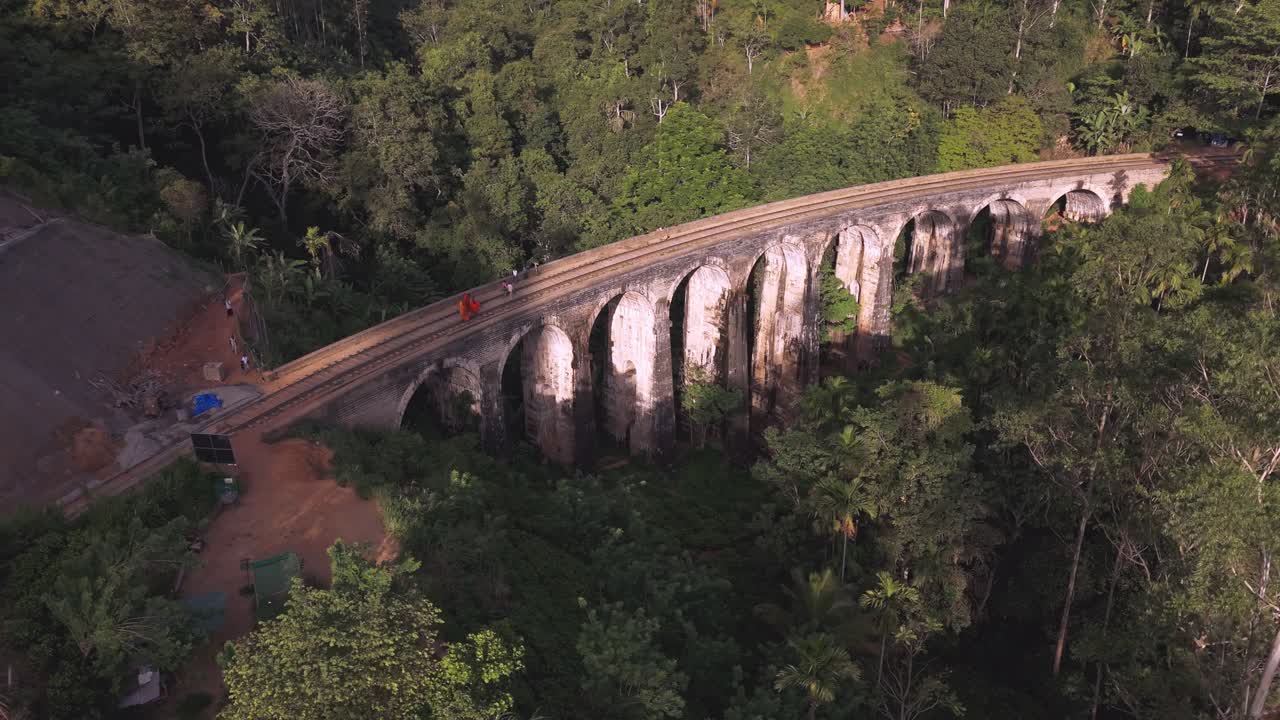 Monks walking over the iconic architecture railway bridge, central Sri Lanka. Drone aerial rotate.