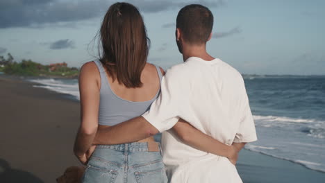 couple hugging waists walking on beach