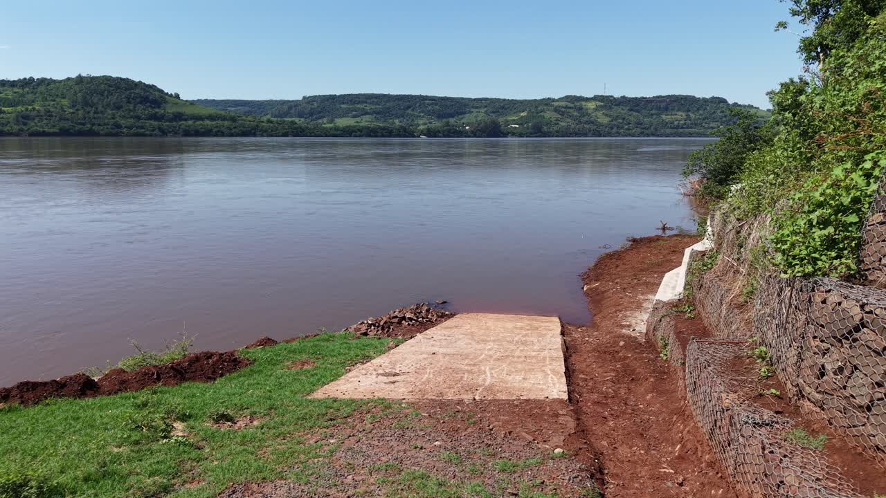 Dynamic drone fly at boat ramp on the Uruguay River in green riverbank environment, Misiones, Argentina