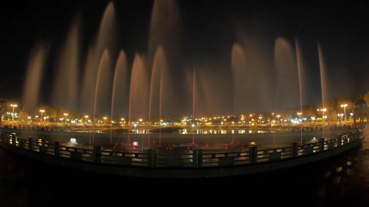 Tall symmetrical fountains glowing under city lights in a quiet park at night