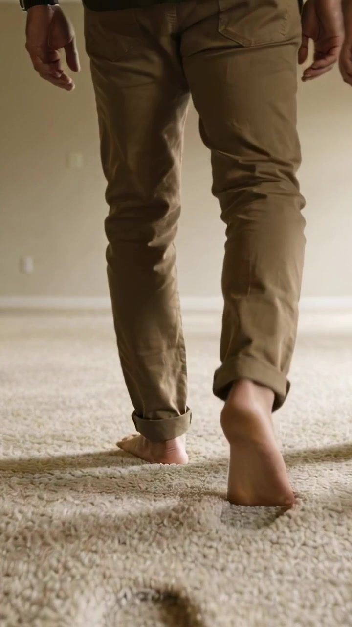 Vertical video: Stepping barefoot adult in cuffed khakis leaving prints on floor in room with watch