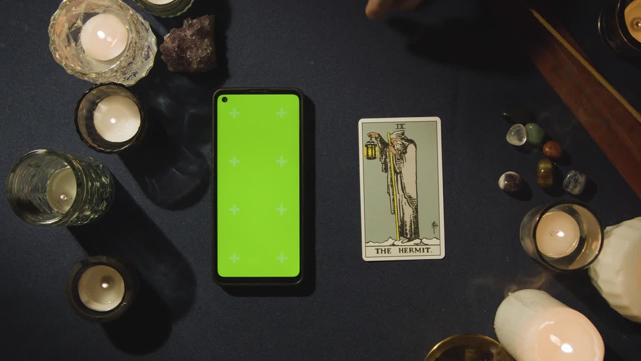 toma aérea de una persona que da lectura de tarot con un teléfono móvil de pantalla verde junto a la tarjeta de ermitaño en la mesa