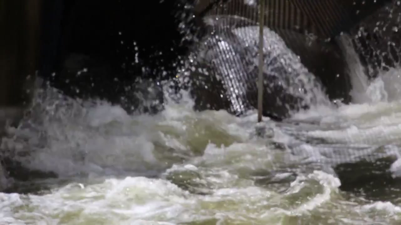 Potente flusso d'acqua industriale si riversa attraverso una griglia di drenaggio metallica con un intenso movimento di schizzi, creando energia dinamica e movimento turbolento in un ambiente umido.
