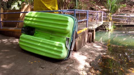 a bright green plastic paddle boat is flipped upside down near a dock by a small lake, surrounded by trees. shot with pan right movement.
