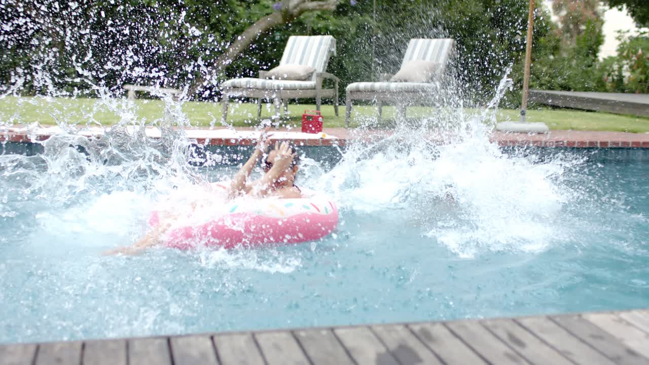 Diverse women in swimwear running, jumping into backyard pool, playing, soaking her on pink float