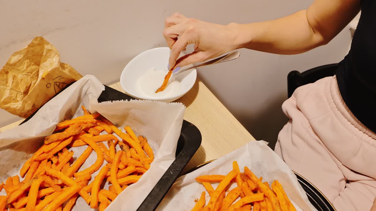 Evening kitchen scene of woman enjoying hot fries with sauce on tiny table