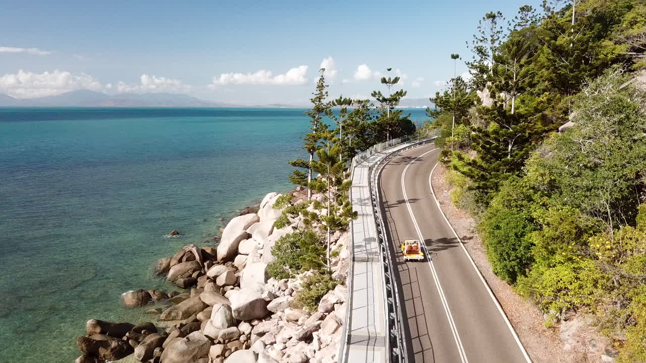 vista aérea de un buggy de playa clásico descapotable abierto conduciendo a lo largo de la carretera costera del acantilado junto a aguas tropicales cristalinas con un cielo azul brillante
