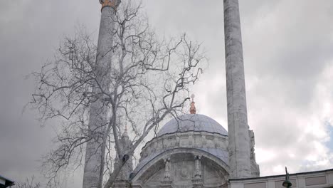 mosque with minarets on background of cloudy sky. action. bare tree on background of mosque in cloudy weather. beautiful white mosque with minarets in gray cloudy weather in autumn