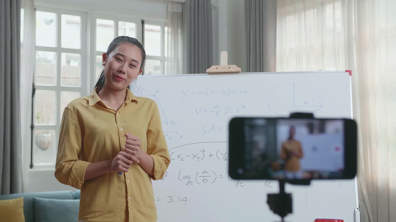 Azjatycka nauczycielka z markerem nagrywa wideo smartfonem, ucząc matematyki w domu.